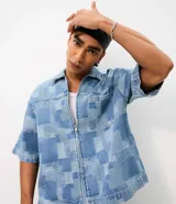 Camisa de jean de algodón con textura jacquard y diseño geométrico, de corte boxy, cuello con solapa, manga corta y cierre frontal con cremallera.