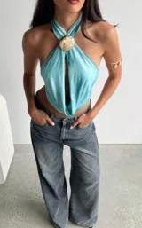 Top halter celeste con abertura en el centro y detalle de aplique con forma de concha dorada en el cuello.
