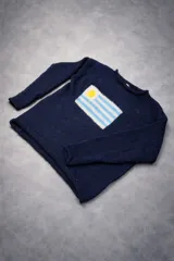 Sweater de tejido de punto en color azul marino, con diseño de la bandera de Uruguay tejida en el frente. Presenta cuello redondo, mangas largas y un corte holgado.