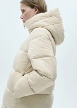 Campera acolchada tipo puffer de color beige, con diseño recto, cuello alto y capucha integrada. Presenta cierre frontal de cremallera doble y bolsillos laterales con cierre.