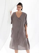 Vestido midi color visón de lino, con cuello en V, mangas 3/4 con botón para sujetar, corte evasé y dos botones decorativos en el frente.