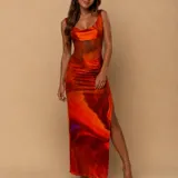 Vestido largo de satén con estampado abstracto en tonos naranja y rojo. Presenta un escote tipo cowl, paneles laterales de microtul transparente en la cintura y una abertura lateral en la falda.