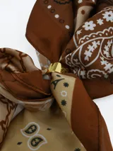 Pañuelo de seda con estampado geométrico en blanco, negro y gris, que incluye un anillo metálico dorado para sujetarlo.