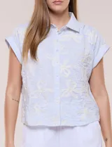 Camisa celeste con bordado floral en color crudo, de corte semi holgado, cuello camisero, manga corta japonesa con dobladillo y cierre frontal de botones.