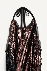 Vestido largo de lentejuelas con cuello halter, espalda descubierta y lazos para atar al cuello. Cuenta con un cinturón de lazo en contraste y diseño bicolor que combina tonos tostados y negros.