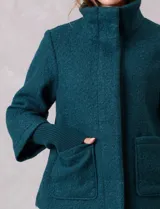 Tapado de tejido bouclé color marrón, con silueta evasé y largo a la cadera. Presenta cuello alto envolvente, cierre frontal oculto con botones a presión y bolsillos frontales de gran tamaño. Sus mangas son 3/4 con corte amplio y puños de tejido rib al tono que se extienden para cubrir las muñecas.