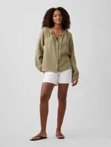 Camisa de muselina color verde militar, de manga larga abullonada, con cuello redondo fruncido y cierre frontal de botones.
