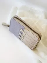 Billetera pequeña de cuero color lila y beige con cierre metálico y detalle de cordones cruzados en el frente.