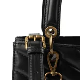 Cartera negra de símil cuero acolchado con diseño de líneas horizontales en forma de V. Tiene acceso con cierre y broches imantados, correa regulable, herrajes dorados y tres compartimentos internos. Se puede usar como bandolera o de mano.