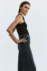 Jean tobillero de denim azul con leve elasticidad, tiro alto y perneras amplias tipo wide leg. Presenta bolsillos delanteros tipo parche con solapa y botones metálicos, además de pliegues marcados al frente y en la espalda.