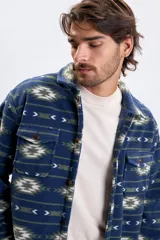 Sobrecamisa de tejido polar con estampa abstracta en tonos azules, verdes y blancos. Presenta cuello camisero, cierre frontal con botones, dos bolsillos frontales con solapa y botones, y un interior afelpado para mayor abrigo.