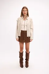 Campera de gamuza color beige con diseño de calados florales en hombros y espalda, cierre frontal y cuello camisero. Presenta un corte relajado y textura suave.