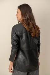 Campera estilo sobrecamisa confeccionada en cuero negro, de corte recto, con cuello camisero y cierre frontal de botones metálicos a presión.