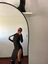 Vestido midi negro de corte ajustado, cuello alto y mangas largas. Presenta una abertura lateral en la falda y largo asimétrico.