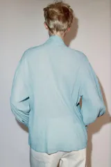 Camisa de rayas finas color amarillo, confeccionada con cuello redondo y lazada en el mismo tejido en el escote. Presenta mangas largas con hombros caídos y puños anchos abotonados.
