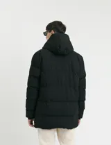 Campera puffer de corte largo, color verde militar, con capucha fija, cierre frontal y puños elásticos internos.