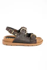 Sandalias de cuero marrón oscuro, con doble tira ancha en el empeine y tira en el talón, todas con hebillas metálicas doradas. Cuenta con suela plana y gruesa de tono tostado con estriado inferior.