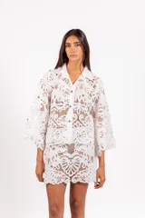 Camisa de molde clásico confeccionada en encaje bordado tipo guipur, color azul, con mangas largas amplias y aplicación de tachas doradas.
