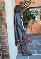 Pantalón de viyela a cuadros en tonos marrón y negro, de corte ancho y recto. Tiene botón en la pretina delantera y elástico en la parte trasera de la cintura.