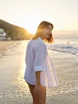 Camisa blanca de lino con cuello clásico, mangas largas y cierre frontal con botones color madera. Presenta detalles de frunces verticales en el frente.