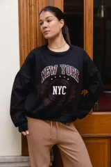 Buzo de felpa negro con diseño estampado en el pecho con las inscripciones 'NEW YORK' y 'NYC', rodeado de detalles gráficos de estilo universitario.