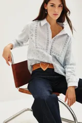 Camisa de algodón con diseño de encaje bordado, cuello clásico y frente con tablas verticales. Presenta mangas largas con puños abotonados y cierre frontal con botones.