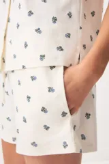 Pijama de algodón color blanco con pequeño estampado floral azul, compuesto por una camisa de mangas cortas con cuello solapa, botones frontales y bolsillo en el pecho, y un short con elástico y lazo ajustable en la cintura.