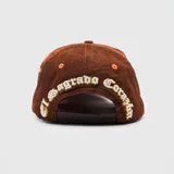 Gorra tipo trucker de pana color marrón, con bordado frontal en relieve y detalle lateral bordado del Sagrado Corazón de Jesús.