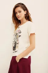 Remera blanca de algodón con cuello redondo, mangas cortas y estampa frontal de una guitarra rodeada de flores y la frase 'your own muse'.
