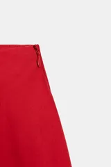 Falda midi de tiro alto y corte en A, color rojo, con bolsillos laterales ocultos y cierre lateral con cremallera.