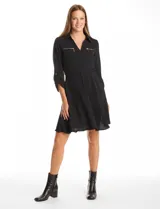Vestido corto de crepe color negro, con cuello solapa y escote en V. Presenta bolsillos simulados con cierre metálico en el pecho, mangas largas regulables con presilla y botón, y cintura elastizada.