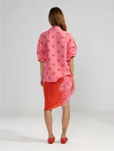 Camisa de manga larga color rosa con rayas verticales rojas y estampado de flores rojas. Con cuello camisero, puños elastizados y lazos regulables en los costados del ruedo.