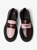 Mocasín de piel vacuna en color negro, con detalles en rosa claro y marrón oscuro en la parte superior. Cuenta con suela de goma gruesa y dentada, y plantilla OrthoLite reciclada.