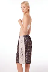 Bermuda unisex de poliéster con estampado de camuflaje y banda lateral color crema con texto en cursiva.