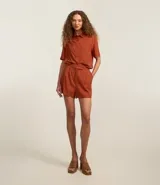 Short corto de mujer confeccionado en mezcla de lino y viscosa, color tostado. Presenta un diseño con pliegues delanteros, bolsillos laterales y un cierre asimétrico.