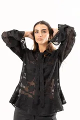 Blusa negra de tejido semitransparente con diseño floral en relieve, cuello alto con lazo frontal y mangas largas con volados en los puños.