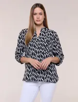 Blusa de calce suelto y caída ligera en color negro con estampado geométrico blanco. Presenta escote en V, cuello mao, abotonadura frontal metálica y bolsillos superiores en el pecho. Cuenta con mangas largas regulables con presilla y botón, ruedo redondeado con tajos laterales y canesú en la espalda.