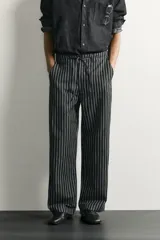Pantalón relaxed fit de mezclilla con mezcla de algodón y lino, con diseño de rayas verticales oscuras y claras. Cuenta con cintura ajustable con cordón, bolsillos frontales, bolsillo cerillero y cierre frontal con cremallera y gancho metálico.