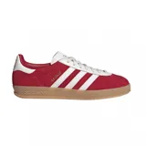 Championes adidas Gazelle Indoor, confeccionados en gamuza color rojo con las icónicas tres tiras laterales y refuerzo en el talón en color blanco. Presenta suela de goma color caramelo y el nombre del modelo en letras doradas en el lateral.