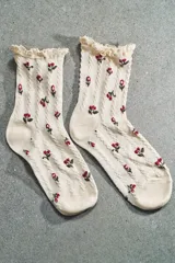 Calcetines marrones con estampado de flores en tonos naranja y beige, confeccionados en hilatura de algodón. Presentan un detalle de tejido con estructura y acabado con puntilla a tono en el borde superior.