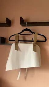 Top corto de ecocuero negro con corte asimétrico y un tirante ancho de ecocuero blanco con textura de piel de cocodrilo. Se ajusta con botones o lazo en la espalda.