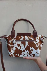 Cartera tipo bolso de mano confeccionada en cuero gamuzado color suela, con solapa de cuero liso y cierre metálico. Incluye doble manija corta y correa larga desmontable.