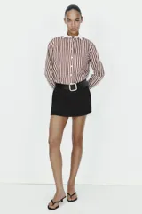 Falda pantalón de tiro medio color negro, con bolsillos delanteros y detalle de cinturón integrado con hebilla metálica dorada. Cierre frontal con cremallera y gancho.