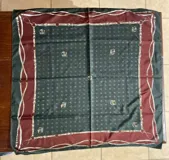 Pañuelo de seda cuadrado con diseño estampado de inspiración ecuestre, con marcos en tonos verde oscuro y bordó, detalles de cinturones, herrajes y cabezas de caballo.