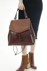 Mochila de cuero vacuno marrón con acabado pulido, solapa en forma de V y costuras decorativas. Cuenta con cremalleras laterales y asas ajustables.