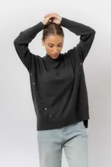 Sweater de tejido de punto color marrón, con cuello alto, corte relajado y terminaciones en rib en puños y cintura. Presenta una hilera de botones metálicos decorativos en uno de los laterales.