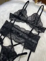 Conjunto de lencería de cuatro piezas en encaje negro. Incluye bralette con breteles regulables, tanga con tiras dobles ajustables en la cintura, portaligas con enganches desmontables y ligas para las piernas.