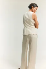 Chaleco largo color blanco hueso, con cuello redondo, cierre frontal con botones dorados, bolsillos delanteros ribeteados y abertura en la parte posterior. Forrado.