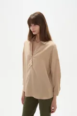 Blusa holgada de poliéster color beige, con cuello camisero, escote en V con botones frontales y mangas largas.