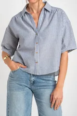 Camisa de manga corta con patrón de rayas verticales en tonos azul y blanco, cuello camisero y cierre frontal con botones.